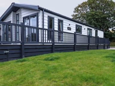 An exterior view of a white and black mobile home with a porch and railing on a grassy lawn