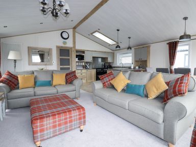 A living area with two grey sofas and a plaid ottoman in front of a kitchen at Beachcliff in Porth