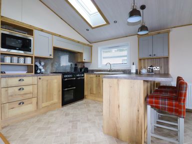 A kitchen with wooden cabinets a black stove a microwave and plaid chairs at Beachcliff in Porth