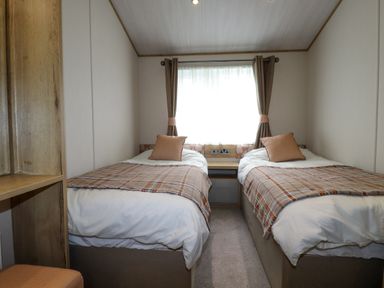 A bedroom with two single beds a small nightstand and a window with curtains at Beachcliff in Porth