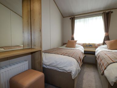 A bedroom with two single beds a window between them a small bedside table and a dressing table with stool at Beachcliff in Porth