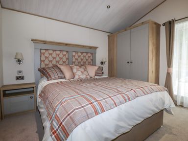 A bedroom with a bed with plaid bedding bedside tables a wardrobe and curtains at Beachcliff in Porth