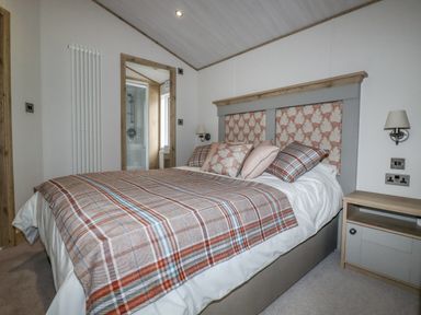 A bedroom with a bed covered with checkered bedding and pillows next to a bedside table and a door leading to a bathroom at Beachcliff in Porth