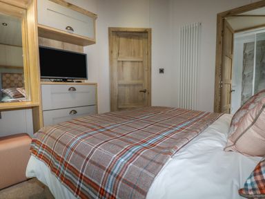 A bedroom with a bed covered in a plaid blanket a wooden door a TV on a dresser and a dressing table at Beachcliff in Porth
