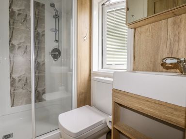 A bathroom with a glass shower enclosure a white toilet and a white sink with wooden cabinets at Beachcliff in Porth