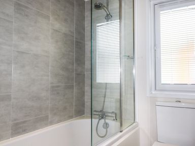 A bathroom with a bathtub shower combination and a window with blinds at Beachcliff in Porth