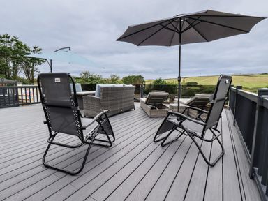 An outdoor patio with reclining chairs umbrellas a sofa and lounge chairs with a view of fields at Beachcliff in Porth
