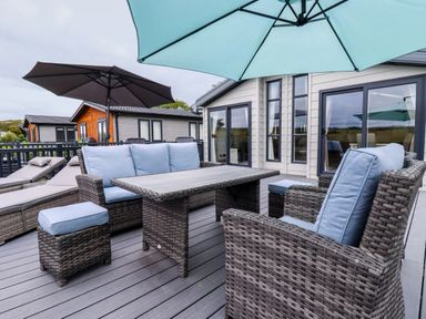 An outdoor patio with wicker furniture and umbrellas on the deck at Beachcliff in Porth
