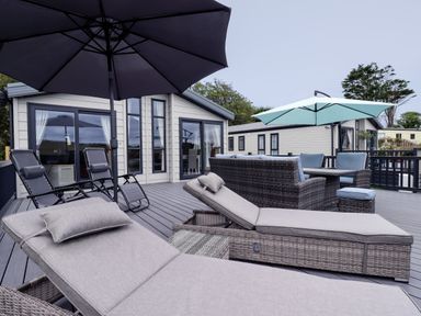 An outdoor deck area with sun loungers umbrellas wicker sofa set and a table at Beachcliff in Porth