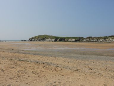 A sandy beach with a rocky headland covered in grass and a clear sky at Beachcliff in Porth