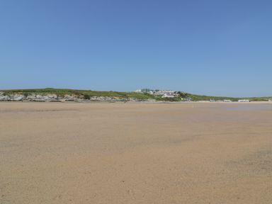 A sandy beach with a rocky coastline and houses on green hills under a clear sky at Beachcliff in Porth