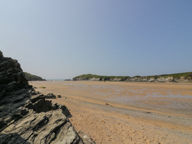 A sandy beach with rocky cliffs and a calm sea under a clear sky at Beachcliff in Porth