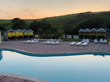 An outdoor pool area with white lounge chairs on a tiled patio and wooden poolside shelters at Beachcliff in Porth