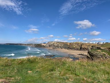 A coastal view with waves hitting the beach and cliffs with buildings on top at Beachcliff in Porth