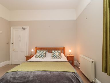 A bedroom with a double bed between two bedside tables with lamps and a radiator near a window with green curtains at Bay Tree House in Seaton Devon