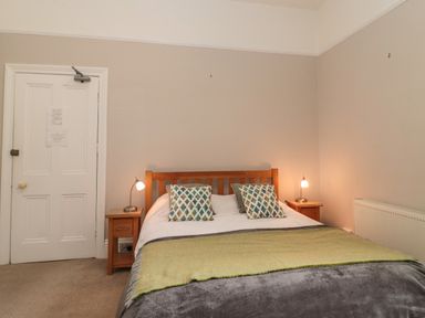 A bedroom with a wooden bed frame two patterned pillows two bedside tables with lamps and a door at Bay Tree House in Seaton Devon