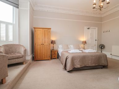 A bedroom with a bed two lamps a wooden wardrobe armchair and a fan at Bay Tree House in Seaton Devon