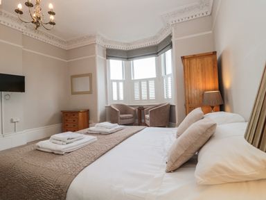 A bedroom with a bed two armchairs a wooden cabinet and a wall mounted television at Bay Tree House in Seaton Devon