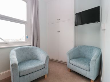 A small room with two blue armchairs a wall-mounted television and a built-in white cupboard by a window at Bay Tree House in Seaton Devon