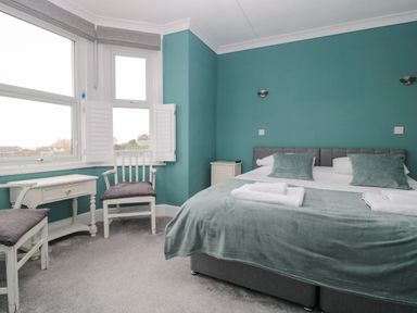 A bedroom with a double bed two chairs small table and large windows at Bay Tree House in Seaton Devon