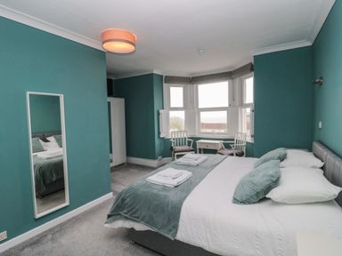 A bedroom with a bed a small table two chairs a wardrobe and a wall mirror at Bay Tree House in Seaton Devon