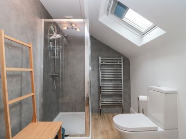 A bathroom with a shower enclosure a toilet a skylight a wooden bench and a heated towel rail at Bay Tree House in Seaton Devon