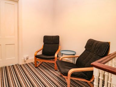 A seating area with two black cushioned wooden armchairs and a small round side table on striped carpet at Bay Tree House in Seaton Devon