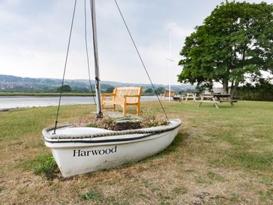 A small boat planter with flowers on grass near benches and picnic tables by a river at Bay Tree House in Seaton Devon