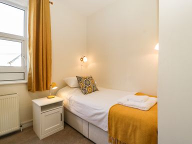 A bedroom with a single bed white bedside cabinet yellow curtain and folded towels at Bay Tree House in Seaton Devon