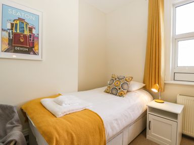 A bedroom with a single bed white nightstand and a window with yellow curtains at Bay Tree House in Seaton Devon