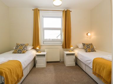 A bedroom with two single beds, bedside tables with lamps, and a window with curtains at Bay Tree House in Seaton Devon