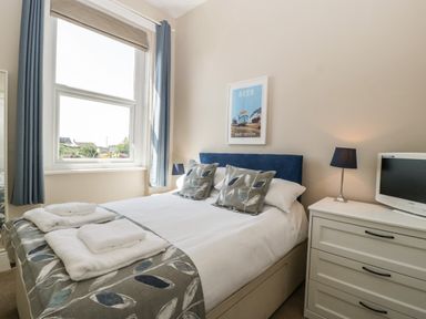 A bedroom with a bed pillows a window a chest of drawers lamp and a television at Bay Tree House in Seaton Devon