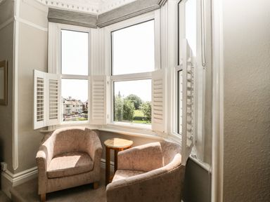 A corner seating area with two chairs and a small round wooden table near bay windows with white shutters at Bay Tree House in Seaton Devon