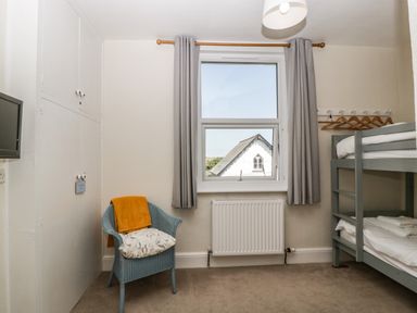 A small bedroom with a bunk bed blue chair with cushion and blanket and window with gray curtains at Bay Tree House in Seaton Devon