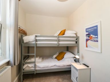 A bedroom with a gray bunk bed pillows and a nightstand with a lamp and remote control at Bay Tree House in Seaton Devon
