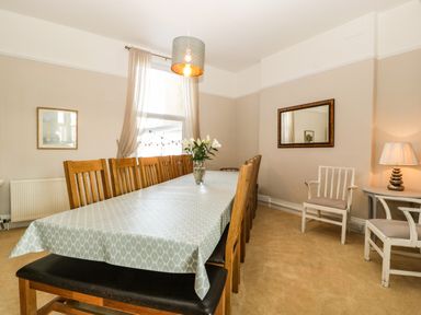 A dining room with a long table and wooden chairs a mirror on the wall and a lamp on a side table at Bay Tree House in Seaton Devon