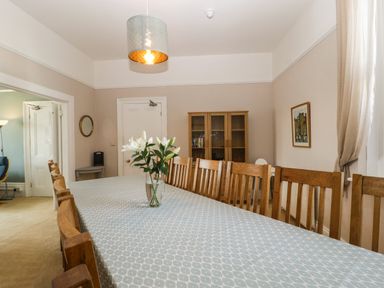 A dining room with a long table covered with a tablecloth and wooden chairs around it at Bay Tree House in Seaton Devon