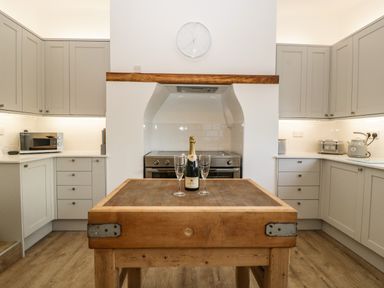 A kitchen with grey cabinets a wooden island a champagne bottle and two glasses on the island at Bay Tree House in Seaton Devon