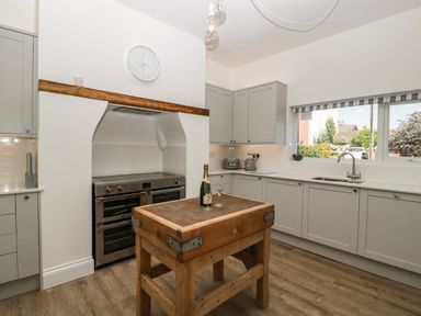 A kitchen with gray cabinets a wooden island a stainless steel oven a clock and a window at Bay Tree House in Seaton Devon
