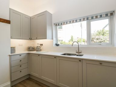 A kitchen with grey cabinets a double sink toaster kettle and a window with striped blind at Bay Tree House in Seaton Devon