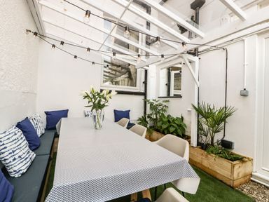 A covered outdoor dining area with a long table, chairs, cushions, plants, and string lights at Bay Tree House in Seaton Devon