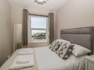 A bedroom with a double bed pillows folded towels a window with curtains and a full length mirror at Bay Tree House in Seaton Devon