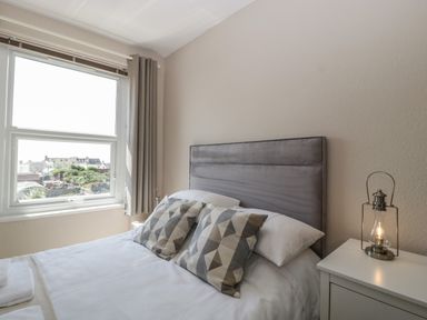 A bedroom with a bed with patterned pillows and a bedside table with a lamp at Bay Tree House in Seaton Devon