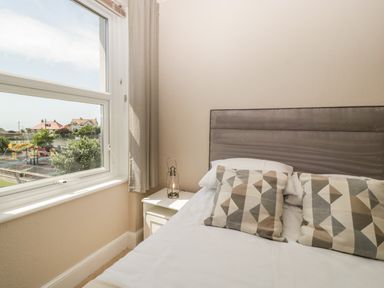 A bedroom with a bed featuring patterned pillows next to a window with a view of a playground at Bay Tree House in Seaton Devon