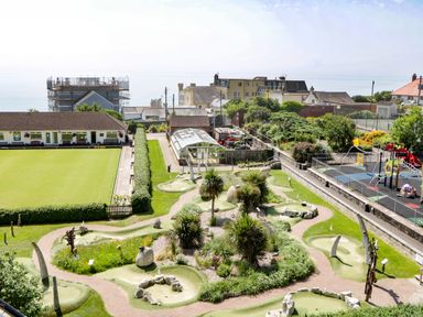 An outdoor mini golf course with pathways and plants next to a bowling green and a playground at Bay Tree House in Seaton Devon