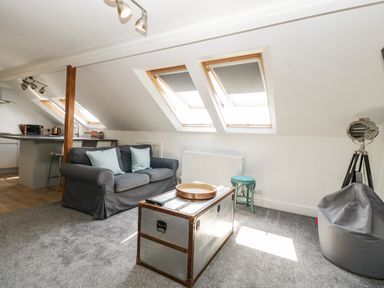 A living area with a grey sofa with pillows a wooden chest coffee table skylight windows and a kitchen area in the background at Bay Tree House in Seaton Devon