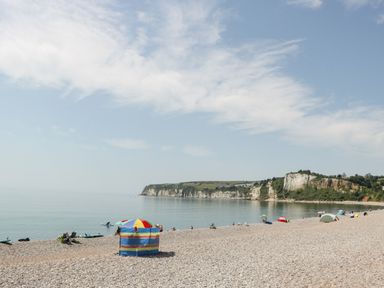 A pebble beach with people and colorful tents by the sea with cliffs in the background at Bay Tree House in Seaton Devon