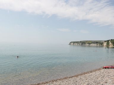 A pebble beach with calm sea water and cliffs in the distance at Bay Tree House in Seaton Devon