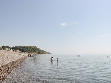 A pebble beach with people swimming and a kayak on the water at Bay Tree House in Seaton Devon