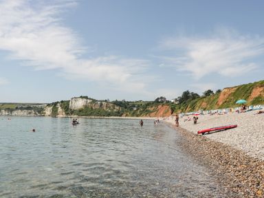 A pebble beach with people swimming and sunbathing near cliffs at Bay Tree House in Seaton Devon